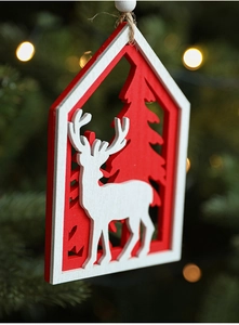 Close-up of wooden house ornament with deer and tree hanging on a lit Christmas tree