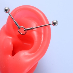 Silver industrial barbell with center ring on a silicone ear model for piercing display