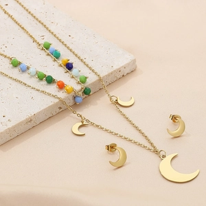 Detail view of multi-layered gold moon necklace and stud earrings on beige stone texture