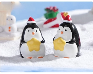 Close-up of two mini Christmas penguin figurines with red hats on faux snow scenery