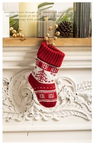 Detail of red knitted Christmas stocking with white tree patterns hanging on a mantel