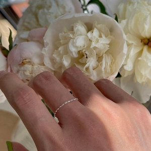 Minimalist silver beaded chain ring worn on hand with a soft peony flower background