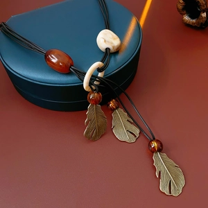 Detail of bohemian necklace with amber beads and brass feather pendants on green leather box