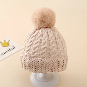 Detail view of cable knit pattern and soft pom-pom on beige winter baby beanie