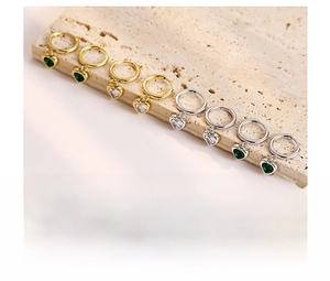 Vue détaillée des boucles d'oreilles cœur dorées et argentées avec zircons émeraude et blancs