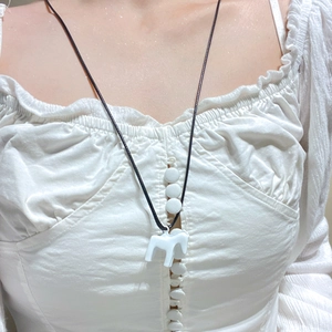 Detail eines weißen Pony-Anhängers an einer schwarzen Kordelkette auf einem Oberteil