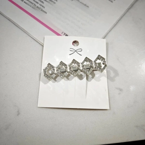 Detail of a silver-tone geometric chain hair clip with sparkling rhinestones on a white card