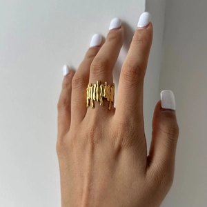Close-up of a wide gold liquid metal ring with an irregular fluid drip design on a finger