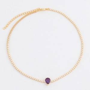 Detail van gouden ketting met een paarse druppel edelsteen en glanzende zirkoon