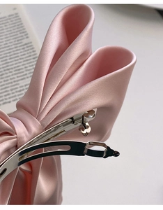 Detail of the pink satin bow hair clip showing the durable metal spring clip mechanism