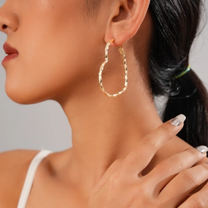 Gros plan d'élégantes boucles d'oreilles cœur torsadées dorées portées par un mannequin chic