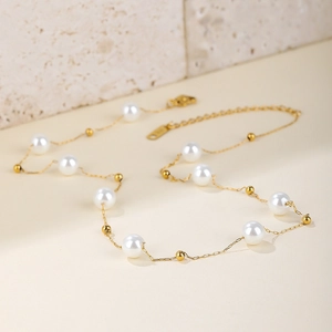 Elegant French style pearl and gold bead necklace in stainless steel on a textured surface