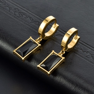 Golden rectangular black gemstone pendant earrings on a textured dark leather background