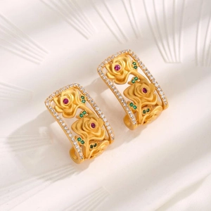 Vintage hollow gold flower earrings with red and green gemstones on white plate