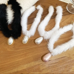 Detail of plush faux fur chokers with elegant waterdrop pearl pendants on wooden surface