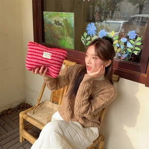 Pink and red striped plush cosmetic bag held by a woman in a sunny outdoor setting