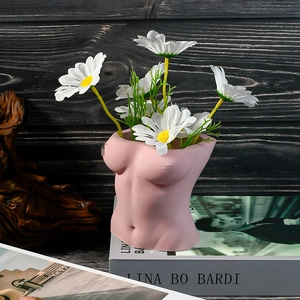 Detalle de jarrón artístico de torso femenino rosa mate con margaritas sobre madera