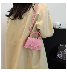 Sac bandoulière rose à texture tressée porté sur un trench-coat beige élégant