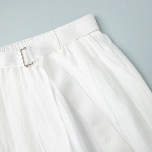 Dettaglio dei pantaloni plissettati bianchi con vita elastica e fibbia in metallo