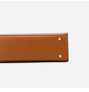 Detail view of brown textured leather bag bottom with gold protective metal feet and black edges