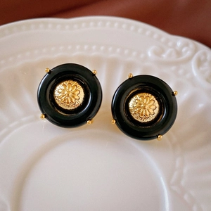 Detail of vintage round black stud earrings featuring a golden floral relief pattern