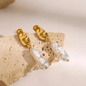 Détail de boucles d'oreilles dorées avec perles baroques sur un support en pierre