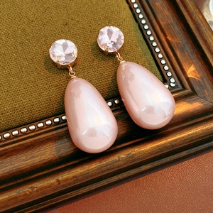 Détail de boucles d'oreilles goutte en cristal rose sur cadre en bois et tissu vert