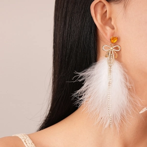 Detail of luxury drop earrings with gold bow, sparkling tassels and white feathers