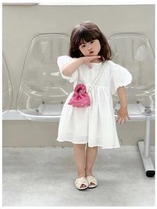 Pink pleated girl's handbag with pearl chain shown on a model wearing a white dress