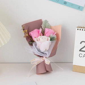 Close-up of mini soap flower bouquet with pink roses and mesh wrap on white table
