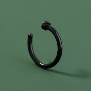 Macro detail of a black polished stainless steel U-shaped nose ring on green background