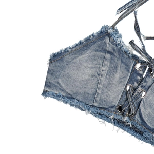 Dettaglio dei bordi sfrangiati e design stringato su un top halter in denim blu lavato