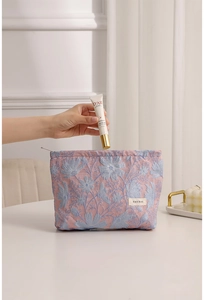 Dettaglio borsa per cosmetici con fiori jacquard e mano che inserisce il trucco