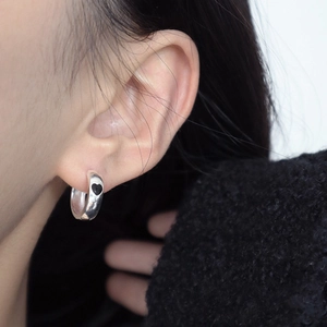 Minimalist silver hoop earrings featuring a black heart drop glaze worn by a model
