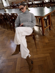 Women's grey high-neck knit sweater with loose white trousers in a vintage library setting