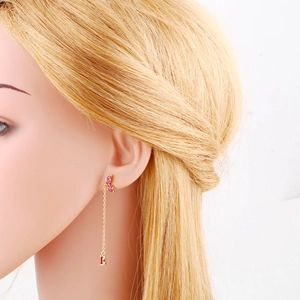 Detail of long gold tassel earrings with pink marquise zircon and red gemstone drop