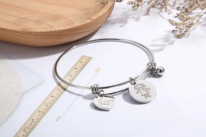 Detail of adjustable stainless steel bangle with Love heart and girl charms on a desk