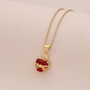Détail macro du collier doré avec pendentif cœur rouge, épines et couronne de flammes