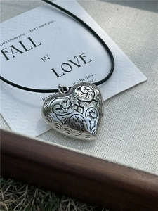 Macro shot of the vintage engraved heart pendant with detailed silver scrollwork on wax cord