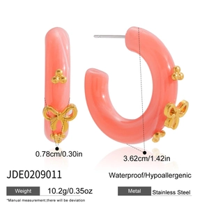 Detail of C-shaped pink hoop earrings with gold bow and bead accents on white background