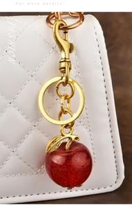 Detail of red glitter apple keychain pendant hanging on white quilted leather handbag