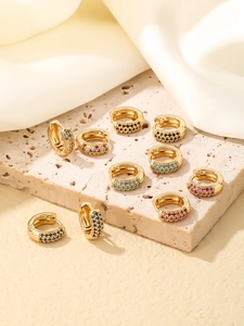 Détail de boucles d'oreilles huggie dorées avec zircone colorée sur tissu en soie