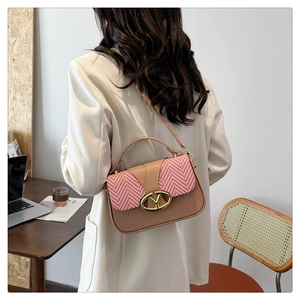 Detail of elegant contrast stitching and gold V-buckle on a small square shoulder bag