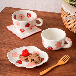Detail shot of ceramic strawberry and floral mugs with a petal-edged tea saucer