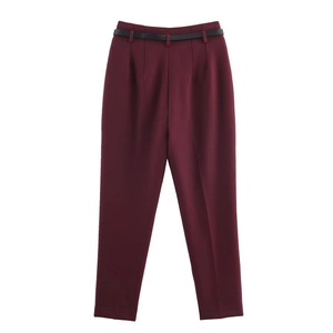 Detailed flat lay of burgundy high-waisted trousers with a slim black belt on white backdrop