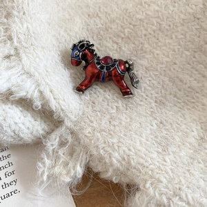 Détail d'une broche cheval en émail rouge avec strass brillants sur un fond en tricot