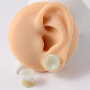 Detailed view of pale green jade stone concave ear gauges worn on a silicone model ear