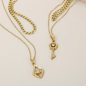 Detail of gold layered necklaces with key and diamond-set eye pendants on flat snake chain