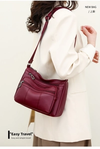 Detail of burgundy soft leather crossbody bag with multiple zipper pockets on a model