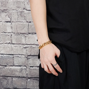 Classic gold Cuban link bracelet for men styled on wrist against a vintage brick wall